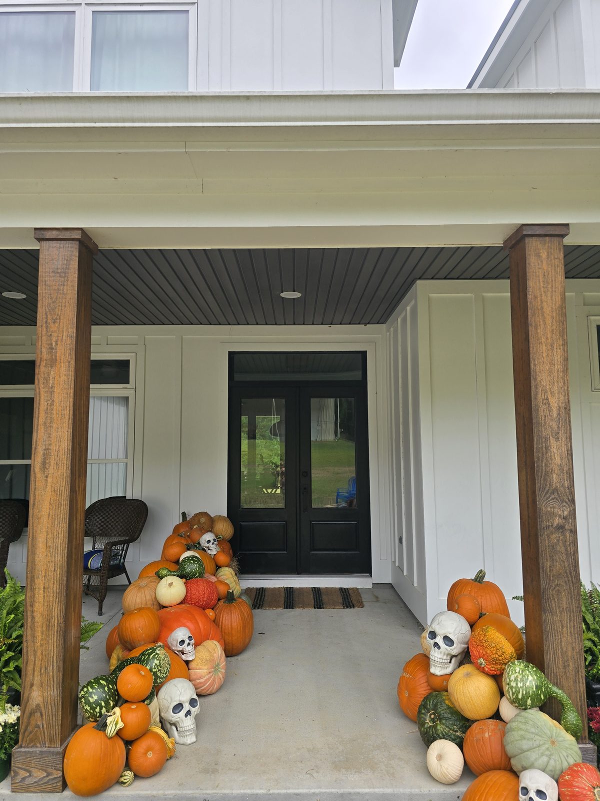 Pumpkins and gourds lining both sides of a farmhouse entry walk with black double doors.