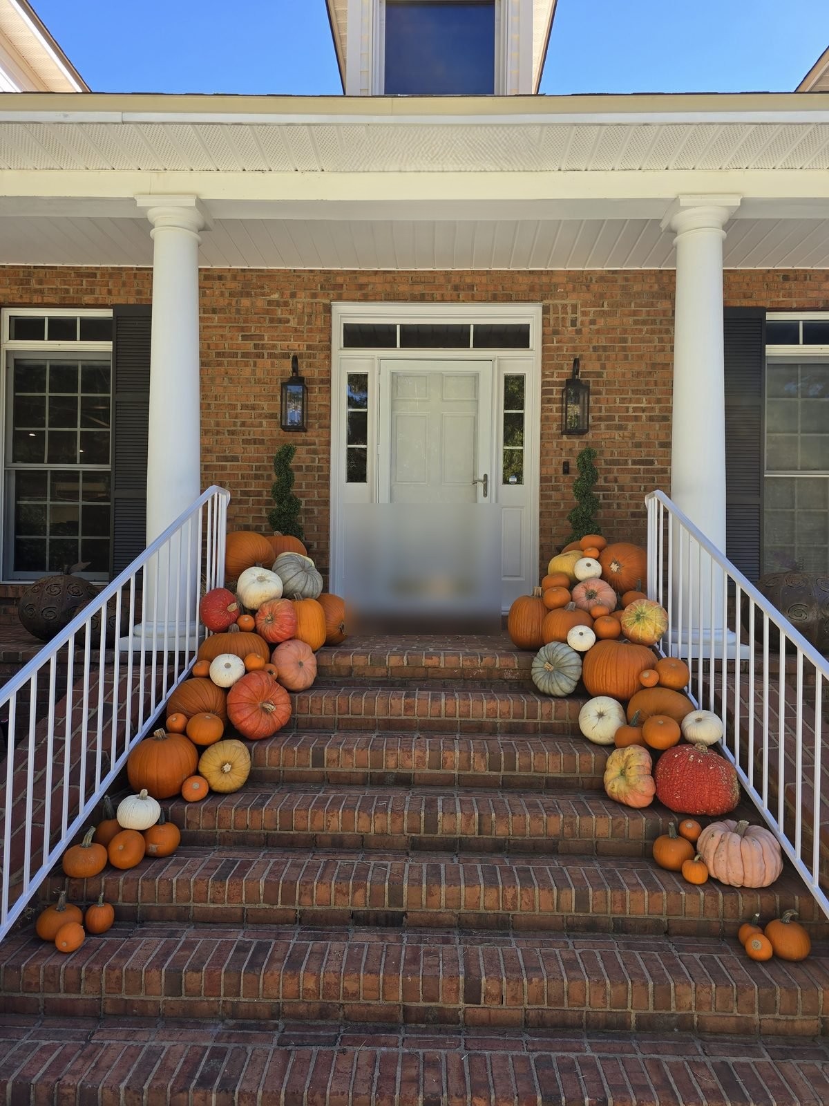 Pumpkins cascading down both sides of a brick front stoop between white columns.