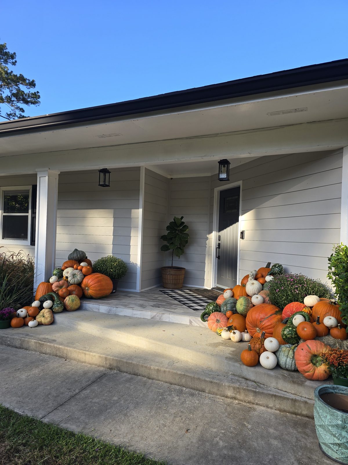 A ranch-style porch with pumpkin piles at both ends and mums planted alongside.